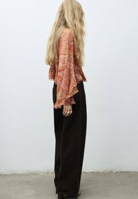 Vloeiend, gestreept topje in tinten van roze en oranje met klokmouwen, gecombineerd met hooggezette donkerbruine wijde broek. Gladde textuur.