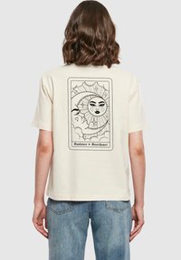 Krémové bavlněné tričko s černým grafickým designem slunce a měsíce, s obdélníkovým okrajem a textem "Sunlover & Starchaser."