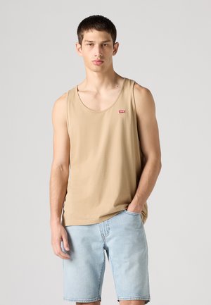 Béžový bavlnený top na ramienka s okrúhlym výstrihom a malým červeným logom Levi's na hrudi, v kombinácii so svetlo modrými džínsovými šortkami.
