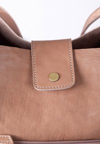 Tan leather bag with a textured surface, featuring a snap closure and stitched accents. Includes a subtle sheen and a zippered compartment.