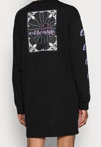 Robe noire à manches longues avec un grand graphisme au dos et des accents violets le long des manches. Confectionnée en coton doux.