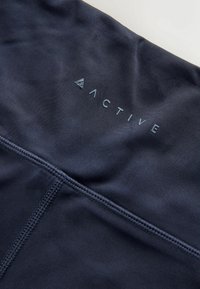 Țesătură bleumarin închis cu cusături cusute și un mic logo și textul „ACTIVE” situat aproape de centru în partea de sus.