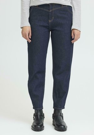 Donkerblauwe denim jeans met een rechte pijpontwerp, voorzien van oranje stiksels, riemlussen en zijzakken. Gekleed met zwarte enkelboots.