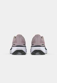 Une paire de chaussures de sport grises et roses vues de l'arrière, affichant des semelles noires crantées et des semelles intermédiaires blanches sur un fond uni.