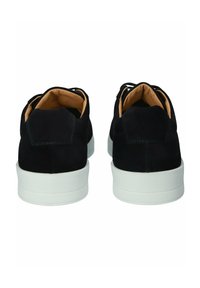 Svarta mockaskor med vita gummisålar, med en enkel design och sömsatta detaljer på hälen och sidan. Snörning.