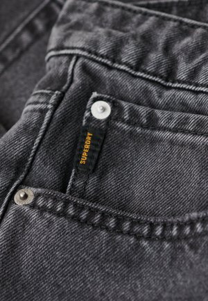 Dark gray denim jeans featuring a prominent Superdry logo tag, metal button hardware, and contrasting stitching along the pockets.