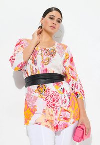 Top colorato con audaci fantasie rosa, arancione e gialla, con scollo a cravatta e maniche a 3/4; abbinato a una cintura nera e una pochette rosa.