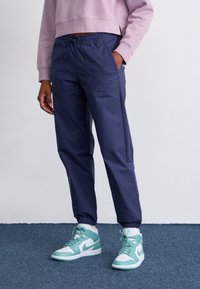 Pantalons de jogging tapered navy avec des poignets élastiques et une taille à cordon de serrage, assortis à des baskets montantes blanches et vert menthe.