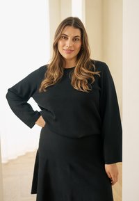 Fekete kötött pulóver hosszú ujjakkal, hozzáillő fekete szoknyával párosítva. Az anyag puha, sima textúrájú.