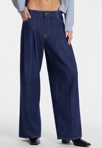 Jeans in denim scuro a vita alta e gamba larga con cuciture visibili, doppie tasche frontali e chiusura con un solo bottone.
