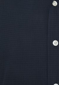 Marineblauw gestructureerd shirt met een knoopsluiting en ronde, lichtgekleurde knopen, en een fijn geruit patroon.