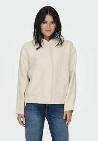 Beige fliisist pullover jakk kõrge kaelusega, esikottide ja mugava lõikega. Sile tekstuur ja lihtne disain.