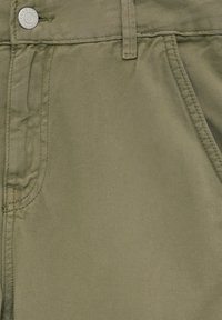 Gros plan sur une poche de pantalon en denim vert olive avec une passant de ceinture et un bouton argenté portant l'inscription "PULL&BEAR DENIM."