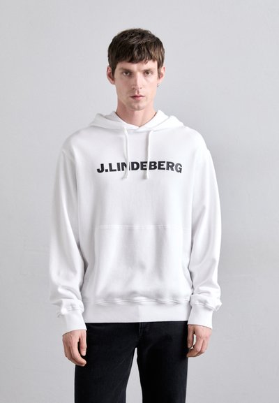 White hoodie with a black "J.LINDEBERG" logo on the front, drawstring hood, and a relaxed fit. Worn with black jeans. Smooth texture.