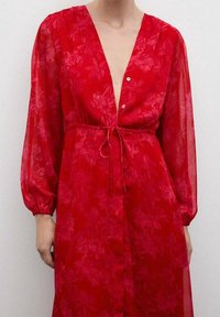 Rotes, transparentes Kleid mit tiefem V-Ausschnitt, elastischem Taillenzug und langen Puffärmeln. Ausgestattet mit einem Blumenmuster und Knöpfen auf der Vorderseite.