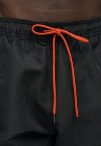 Gros plan de shorts noirs à taille élastique avec un cordon orange vif noué en nœud sur la taille d'une personne.