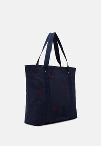 Sac en velours côtelé bleu marine avec des poignées doubles et de petits logos rouges brodés dispersés sur le tissu.