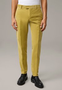 Slanke, mosterdgele broeken van gestructureerde stof, met een vlakke voorkant, riemlussen en zijzakken, gecombineerd met zwarte loafers.