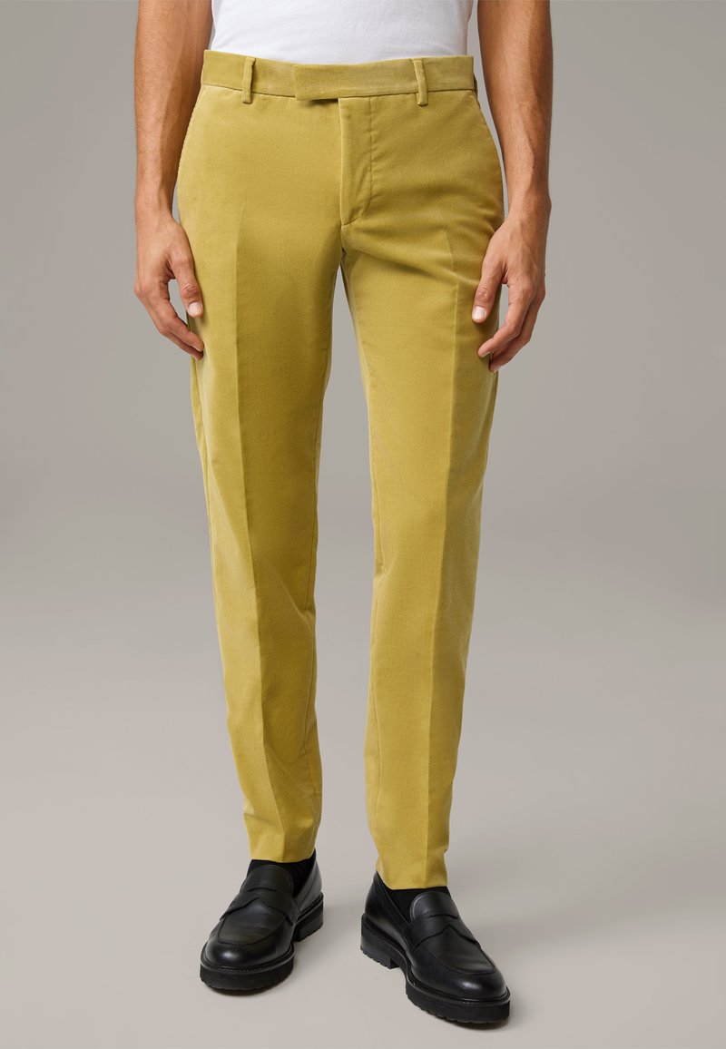 Slanke, mosterdgele broeken van gestructureerde stof, met een vlakke voorkant, riemlussen en zijzakken, gecombineerd met zwarte loafers.