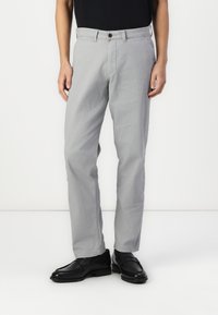 Pantalones de algodón grises con un corte recto, que cuentan con un cierre frontal con botón y bolsillos laterales, combinados con zapatos de cuero negros.