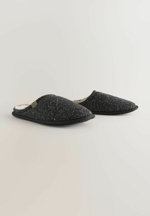 Zapatillas negras de tipo slip-on con un upper de punto texturizado, forro suave y suela acolchada. Presenta un sutil acento de logo en el lateral.