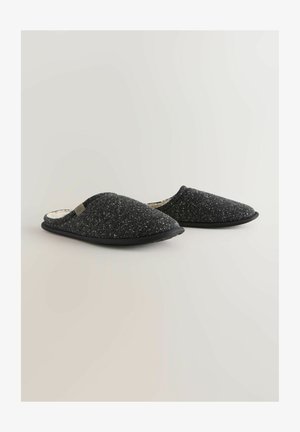 Zapatillas negras de tipo slip-on con un upper de punto texturizado, forro suave y suela acolchada. Presenta un sutil acento de logo en el lateral.