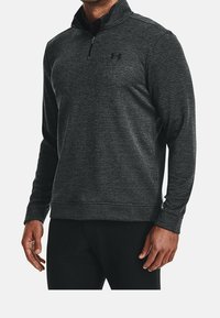 Pullover a maniche lunghe a righe nere con colletto zip e logo sul petto, caratterizzato da una texture liscia e un design aderente.