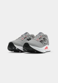 Baskets de sport grises avec un dessus texturé, un logo noir, des accents roses au talon et une semelle blanche et noire.