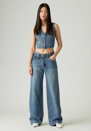 Gilet in denim con bottoni frontali, abbinato a jeans a gamba larga con vita legata e lavaggio blu chiaro. Tessuto morbido e vestibilità rilassata.