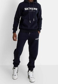 Ensemble sweat à capuche et pantalon de survêtement bleu marine avec le logo blanc « SIXTH JUNE ». Le sweat à capuche est doté d'une poche frontale, de cordons de serrage et de poignets élastiques.