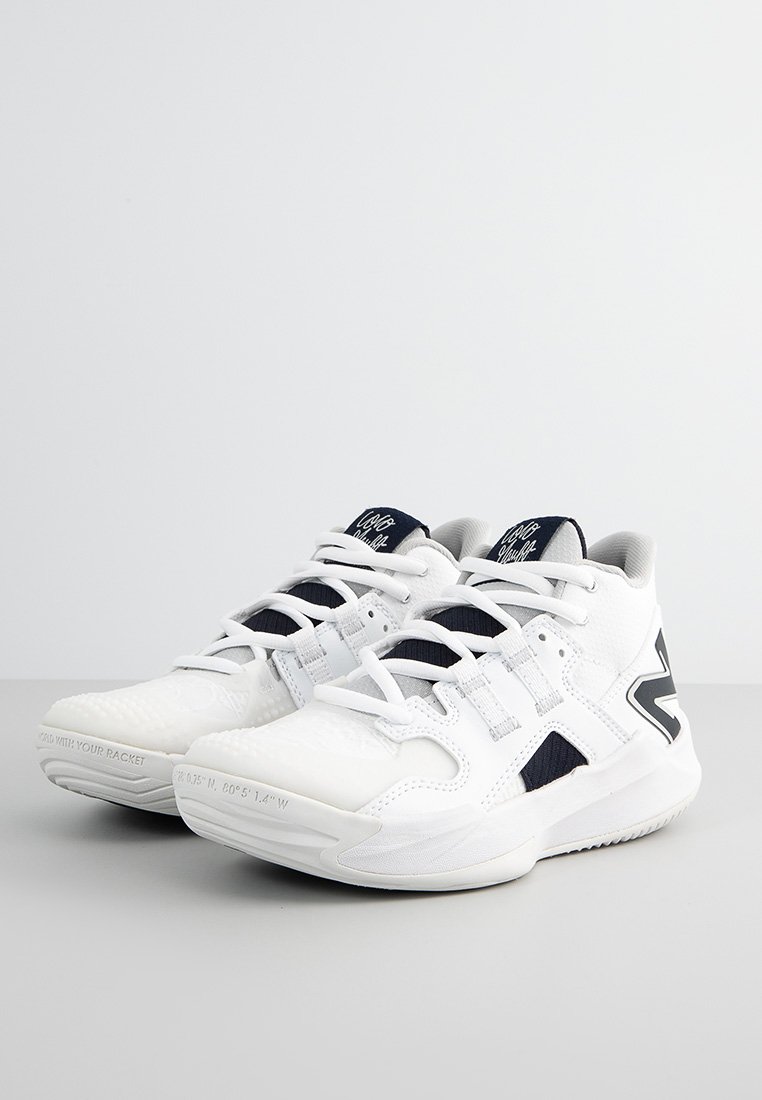 Une paire de baskets blanches avec des accents en tissu noir, un design à lacets et des semelles épaisses texturées, placée sur une surface grise.
