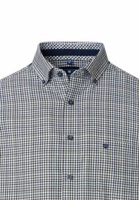 Een overhemd met knoopjes in een marineblauw en crèmekleurig vichypatroon, met een klassieke kraag en een klein zakje met logodetail. De stof is lichtgewicht en geweven.
