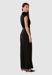 Svarte jumpsuit med tettsittende liv, utsvingte bukser og glatte satengdetaljer. Stylet med svarte spisse sko og minimale tilbehør.