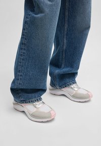 White and gray athletic shoes with pink accents, textured mesh and smooth synthetic materials, paired with loose blue denim jeans.