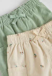 Två par vävda shorts: ett par i dämpad grön med elastisk midja och rosett, det andra i krämfärg med blommönster och ficka.