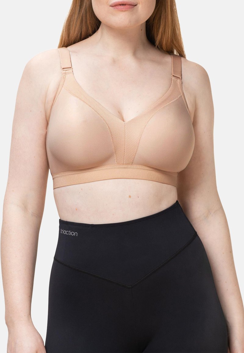 Beige bra, jossa on verkko design, sileä rakenne ja säädettävät hihnat. Yhdistettynä korkeavyötäröisiin mustiin legginsseihin, joissa on matala vyötärö.