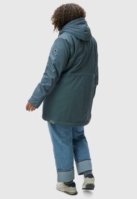 Watershield parka v tmavě modré barvě, s kapucí, odolnou tkaninou a střední délkou, v kombinaci se širokými džíny a teniskami.