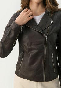 Giacca da moto in pelle marrone con design aderente, zip anteriore asimmetrica e dettagli in metallo argentato. Tasche con zip sui lati.