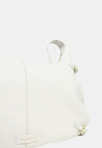 Borsa a spalla in pelle bianca con finitura testurizzata, caratterizzata da un delicato dettaglio di cucitura e accenti in metallo dorato. Etichetta del marchio visibile.
