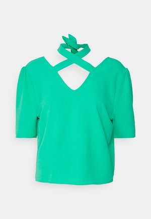 Groen topje met korte mouwen, opgepofte schouders en gekruiste halternekbandjes die aan de achterkant zijn gestrikt.