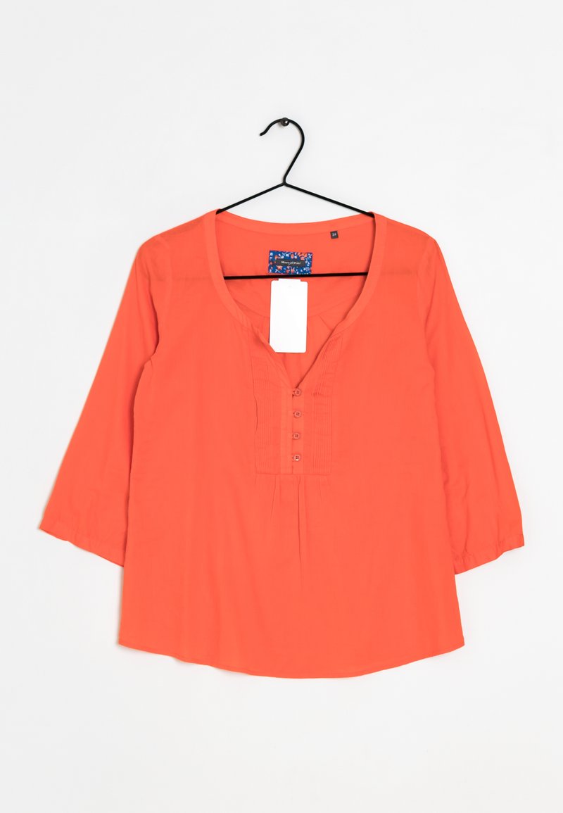 Blouse à manches longues orange vif avec un col en V, quatre boutons et une coupe ample, suspendue à un cintre noir sur un fond blanc.