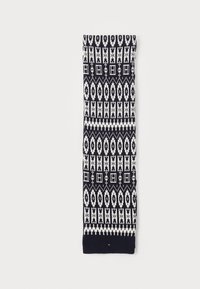 Écharpe en tricot avec un motif géométrique bleu marine et blanc, présentant des formes allongées et des accents carrés, terminée par un bord tricoté uni.