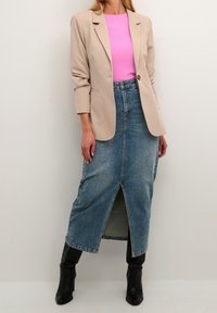 Blazer beige, top de canalé rosa y falda de mezclilla azul con una abertura en el frente. Botas negras hasta la rodilla completan el atuendo, que presenta un look casual y en capas.