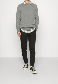 Grå tröja, mönstrad skjorta med krage, svarta byxor och svarta sneakers med vita sulor. Stickad textur med en avslappnad passform.