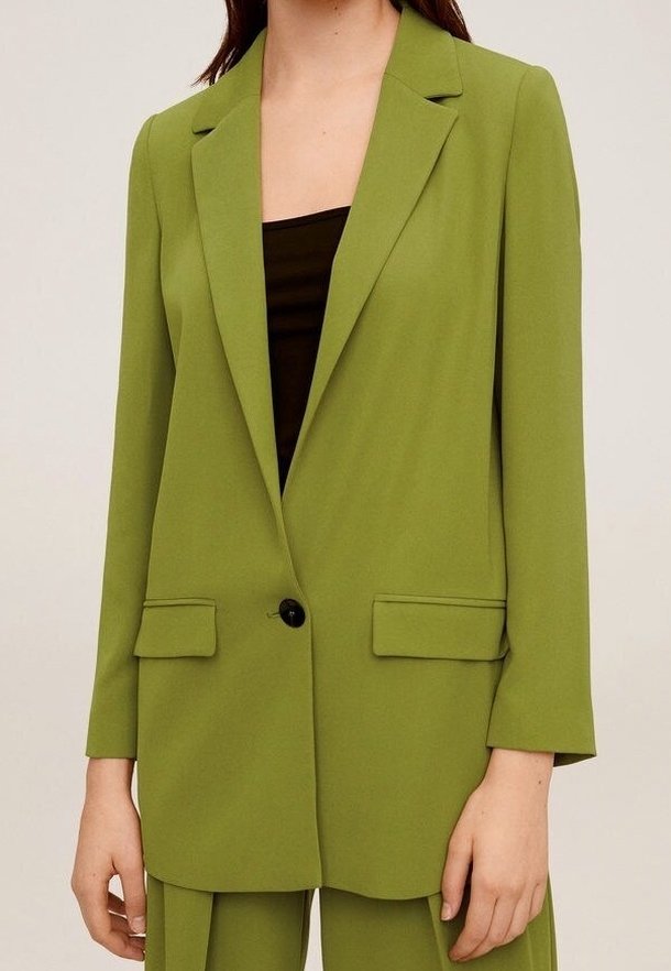 Femme portant un blazer vert olive à un bouton avec des revers crantés et des poches avant à rabat, associé à un pantalon assorti et un haut noir.