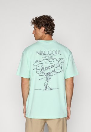 T-shirt in cotone verde menta con una stampa grafica di un albero e un golfista sul retro, con il testo "Nike Golf" e frasi sotto l'illustrazione.