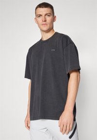 Dark gray oversized t-shirt made of cotton, featuring short sleeves, crew neck, and a small logo on the left chest. Smooth texture.