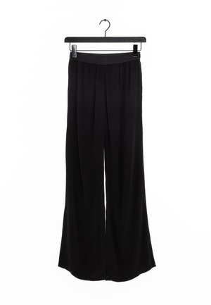 Schwarze weite Hosen aus weichem Stoff, mit einem elastischen Bund, hängen an einem schwarzen Plastik-Hosenbügel vor einem weißen Hintergrund.