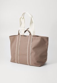 Canvas draagtasje in een gedempte bruine kleur, voorzien van witte accentstrepen en twee stevige crème hengsels voor gemakkelijk dragen.