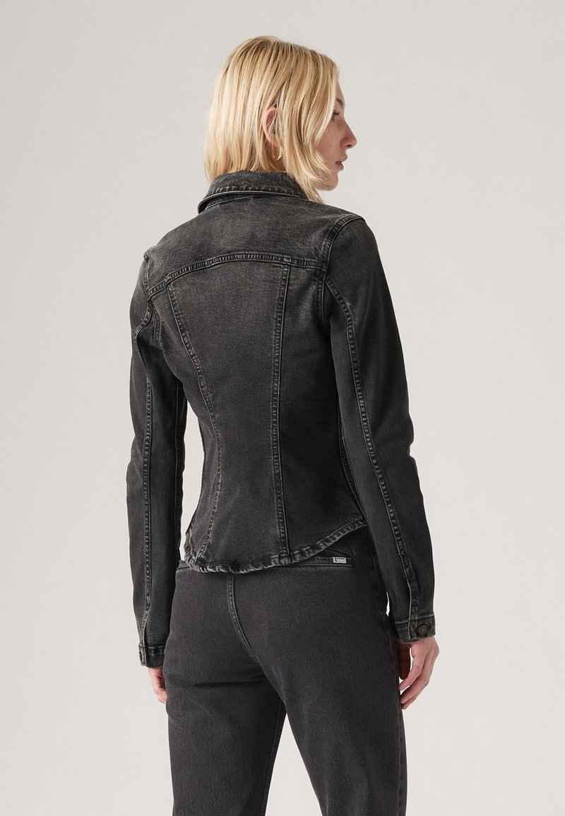 Schwarze Jeansjacke mit einer figurschmeichelnden Passform, subtiler Textur und spitzem Kragen. Verfügt über einen abgerundeten Saum und sichtbare Nähte.